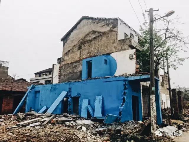 △ 這棟建筑是臨江最近的半拆遷建筑物的遺留，沅江和堤壩成為了展覽的天然背景。創(chuàng)作團(tuán)隊(duì)對(duì)這棟建筑進(jìn)行了半涂裝，將符號(hào)性的沅水曲線與拆遷進(jìn)行中的建筑立面進(jìn)行意義的疊造，它們共同觸發(fā)了場(chǎng)所空間多元語(yǔ)境的生成，把拆遷這種暫時(shí)破壞性、干擾性的介入行動(dòng)與沅水右岸發(fā)展的未來(lái)性、美好性緊密融合。